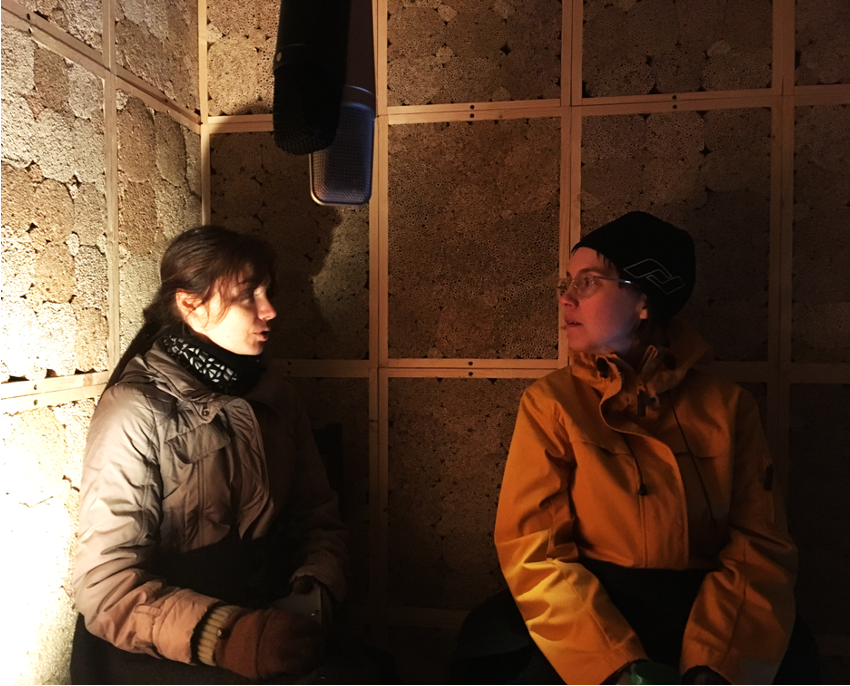 Two people inside a dimm-lighted wooden structure talking